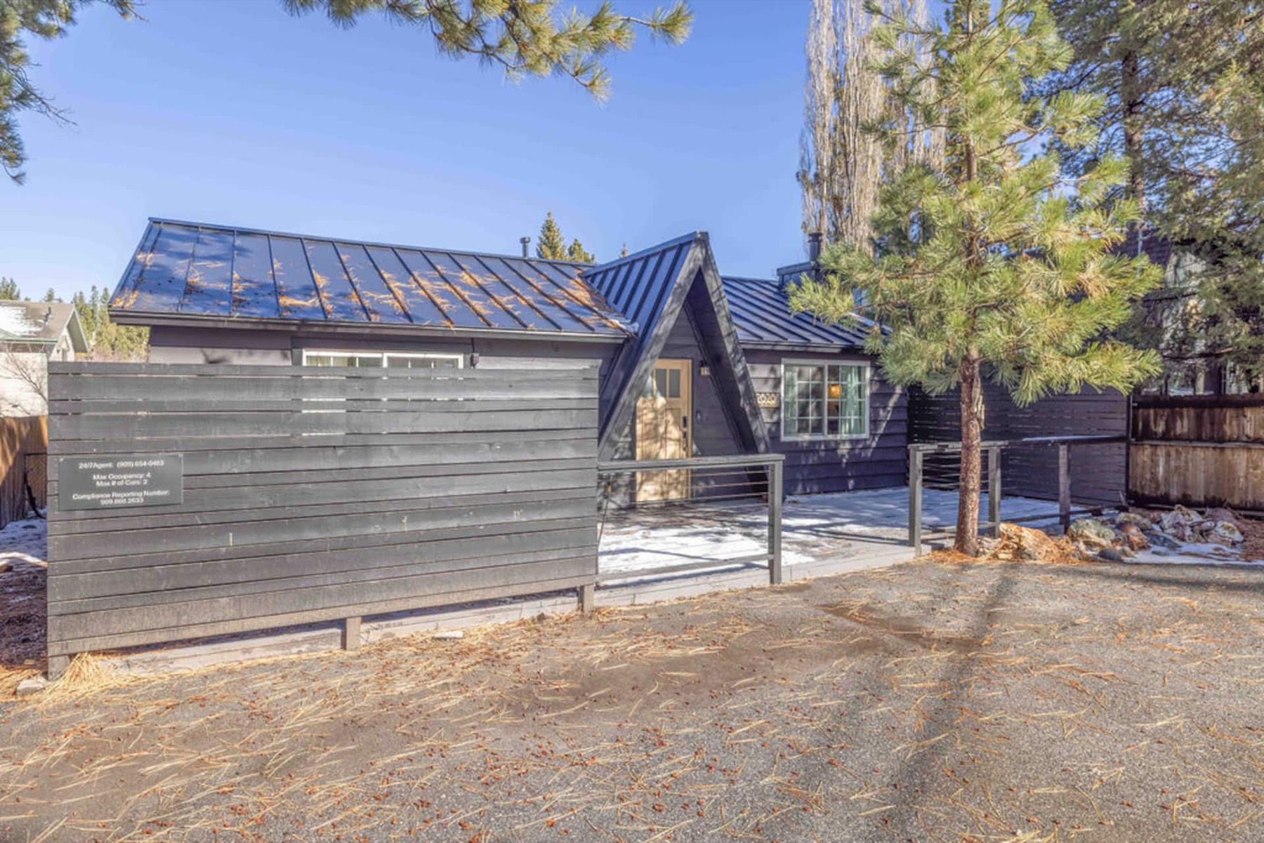 Shadow Ridge Chalet seen from the drive on a clear winter morning — dark board siding, a steep A-frame entry and a standing-seam metal roof under tall Jeffrey pines